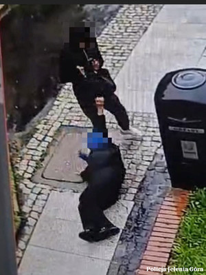 Stopklatka z nagrania. Starsza kobieta leży an chodniku, obok stoi mężczyzna, który wyrwał jej torebkę.