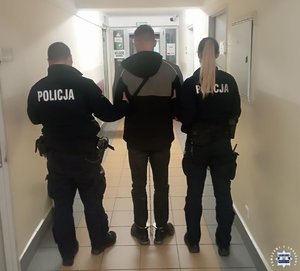 Policjant i policjantka z zatrzymanym na korytarzu.