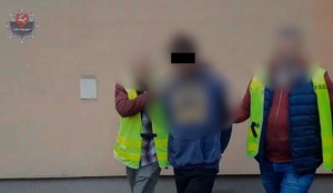 Dwaj policjanci prowadzą zatrzymanego mężczyznę.
