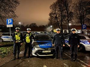 czterech policjantów stoi obok radiowozu.