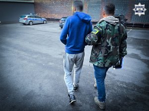 Policjant prowadzi zatrzymanego przez plac.