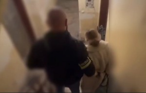 Policjant prowadzi zatrzymaną kobietę.