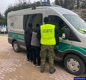 Funkcjonariusz straży granicznej stoi przy samochodzie z dwoma nielegalnymi imigrantami.