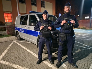 Dwaj policjanci stoją przed radiowozem policyjnym.