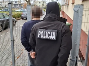 Policjant z zatrzymanym mężczyzną zakutym w kajdanki.