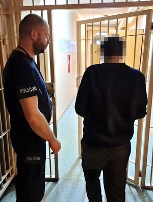 Policjant z zatrzymanym mężczyzną zakutym w kajdanki.