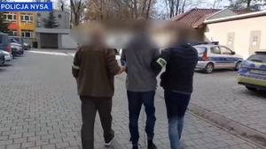 Dwaj policjanci prowadzą zatrzymanego mężczyznę zakutego w kajdanki.