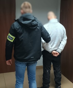 Policjant z zatrzymanym w kajdankach.