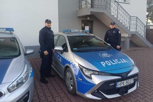Dwaj policjanci stoją przy radiowozie.