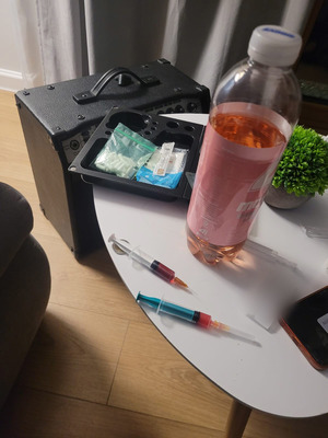 Płyn w butelce, środki w woreczki i dwie napełnione strzykawki z igłami.