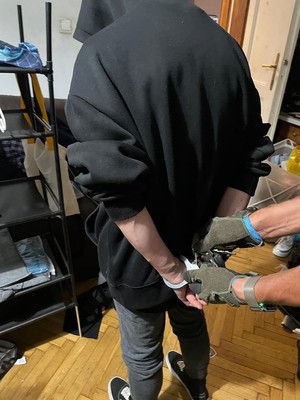 Widoczne dłonie zakładające kajdanki osobie na trzymane z tyłu ręce.