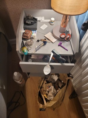 Stolik nocny z fajkami, igłami, strzykawkami i łyżeczką do przypalania.