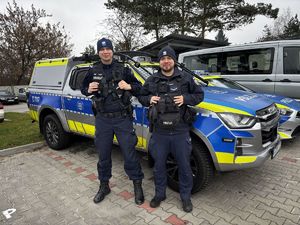 dwóch policjantów stoi przy radiowozie.