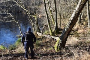 Policjant stoi nad zbiornikiem wodnym w lesie.