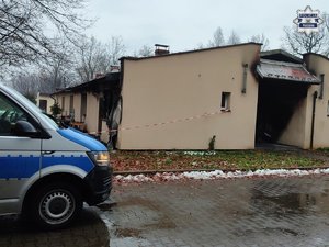 Fragment radiowozu i budynek, w którym wybuchł pożar.