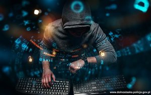 Mężczyzna w kapturze przy dwóch klawiaturach komputerowych.