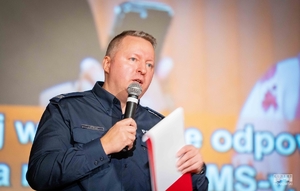 Policjant z mikrofonem w dłoni przemawia do uczestników inauguracji kolejnej odsłony akcji #ZnamTeNumery.