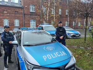 Dwoje umundurowanych policjantów przy radiowozie.
