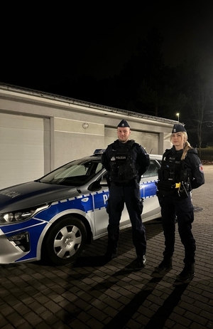 Policjant i policjantka przy radiowozie.