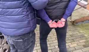 Zatrzymany mężczyzna w kajdankach prowadzony przez policjanta.