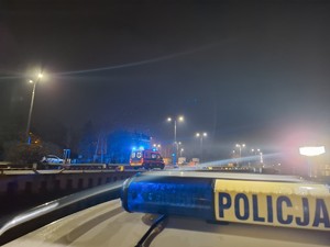 Pora nocna. Na nadbrzeżu stoi karetka pogotowia. Na pierwszym planie sygnalizator z napisem Policja.
