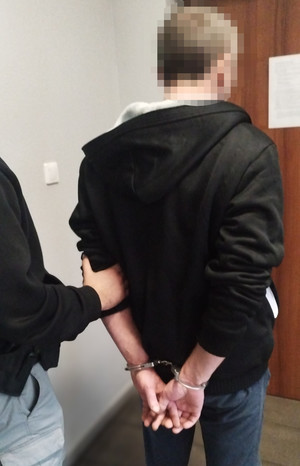 Mężczyzna zakuty w kajdanki prowadzony przez policjanta.