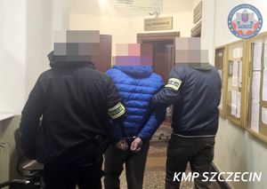 Dwaj policjanci prowadzą przez korytarz mężczyznę zakutego w kajdanki.