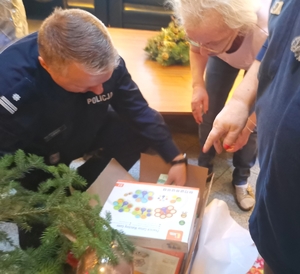Policjant z Biura Prewencji KGP i seniorzy podczas otwierania paczek świątecznych.