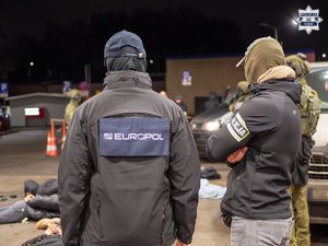 Zdjęcie przedstawia trzech funkcjonariuszy odwróconych plecami, jeden z nich posiada bluzę z napisem Europol, drugi natomiast opaskę z napisem Policja.
