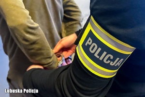 Policjant zakłada zatrzymanemu kajdanki na ręce trzymane z tyłu.