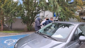 Dwaj policjanci z zatrzymanym mężczyzną przy samochodzie osobowym.