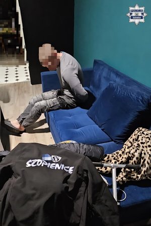 Zatrzymany siedzi na wersalce zakuty w kajdanki.