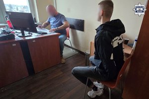 Policjant siedzący przy biurku przesłuchuje zatrzymanego mężczyznę siedzącego na krześle.