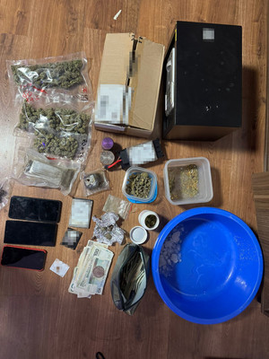 widać wagę, narkotyki w woreczku foliowym i zgrzewnicę. białe kryształki w worku foliowym, następnie dłoń w gumowej rękawiczce przekłada worki z marihuaną w kartonie. radiowóz, policjanta, który zakłada kajdanki zatrzymanemu, który leży na ziemi, następnie widok na pomieszczenie, w którym są paczki i worki z narkotykami, leżący luźno susz i półki na których są różne przedmioty. W pomieszczeniu panuje rozgardiasz.