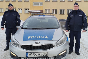 Dwaj policjanci stają obok radiowozu.
