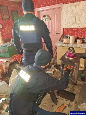 Policjant rozpala ogień w piecu, obok stoi drugi policjant.