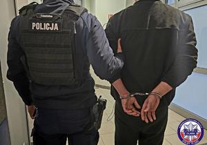 Policjant prowadzi zatrzymanego skutego w kajdanki.