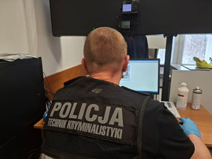 Policjant technik kryminalistyczny siedzi na przeciwko ekranu komputera.