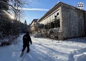 Policjant idzie do pustostanu. zima. wokół leży śnieg.