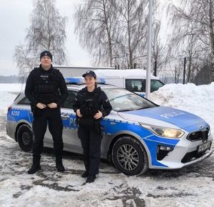 zima, policjantka i policjant pozują do zdjęcia, w tle stoi radiowóz.