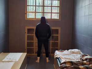 Mężczyzna stoi odwrócony tyłem w pomieszczeniu dla osób zatrzymanych.