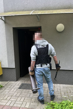Funkcjonariusz CBŚP stoi przed wejściem do budynku mieszkalnego.