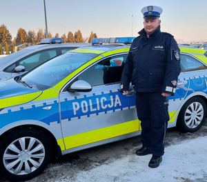 Policjant stoi przy radiowozie.