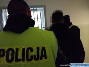 Zatrzymany z policjantem, który ubrany jest w żółtą kamizelkę z napisem Policja na plecach.