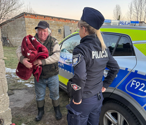 Policjantka przy radiowozie, mężczyzna trzyma koc w rękach.