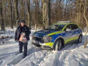 Dzielnicowa z siatką z jedzeniem stoi w śniegu przed radiowozem.