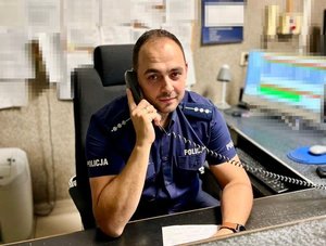 policjant siedzi przy biurku i trzyma przy uchu telefon.