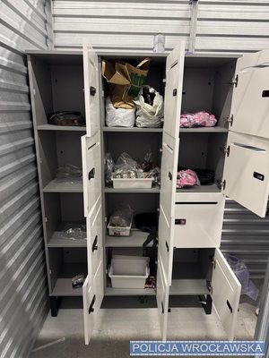 Szafka w magazynie z otwartymi drzwiczkami. W skrytce foliowe kolorowe opakowania zawierające środki odurzające.