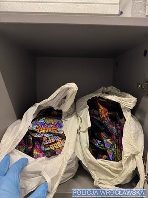 Szafka w magazynie z otwartymi drzwiczkami. W skrytce foliowe kolorowe opakowania zawierające środki odurzające.