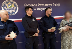 policjanci stoją na tle napisu Komenda Wojewódzka Policji w Augustowie.